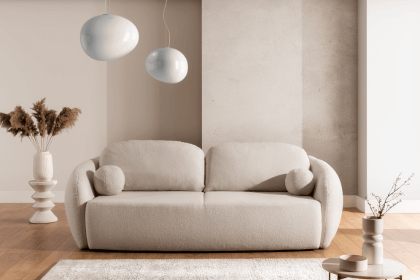 Nowoczesna sofa boucle w jasnym kolorze o miękkiej formie w minimalistycznym salonie z naturalnymi akcentami i dekoracjami.