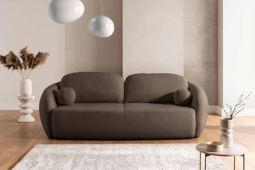 Brązowa sofa o obłych kształtach w jasnym salonie z minimalistycznymi dodatkami i nowoczesnym oświetleniem