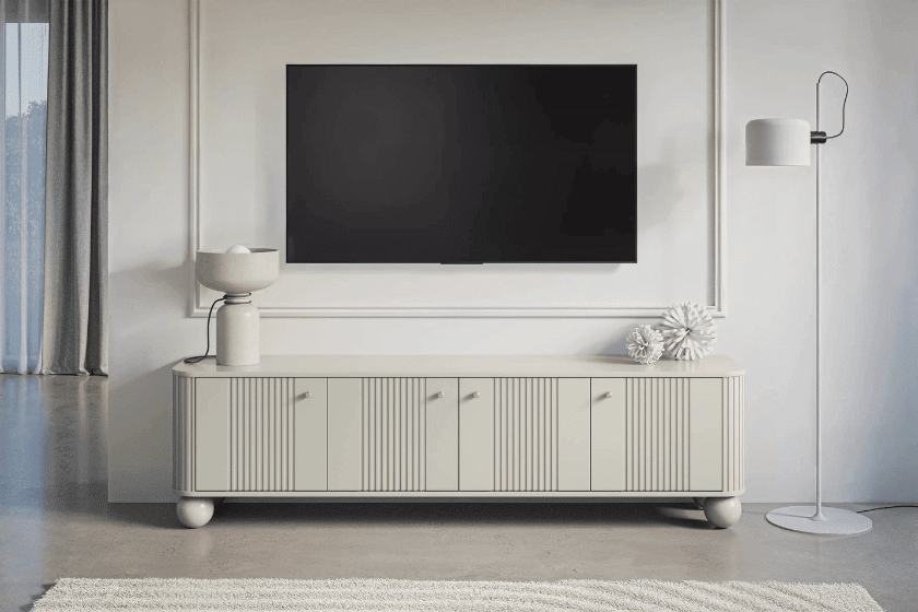 Jasna szafka RTV z pionowym frezowaniem w eleganckim salonie z telewizorem zawieszonym nad nią na ścianie.