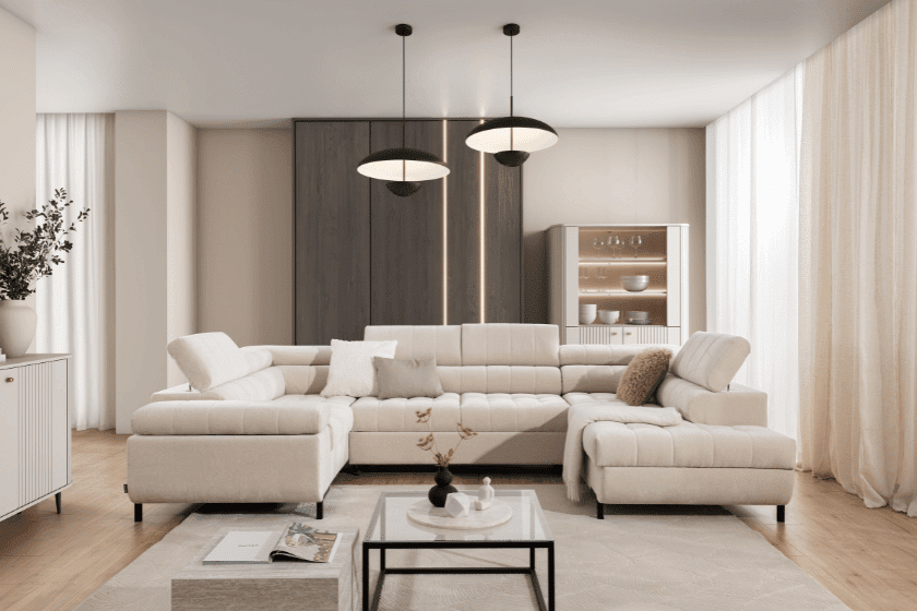 Jasny, nowoczesny salon z beżowym narożnikiem, drewnianą szafką, dużymi oknami oraz minimalistycznymi lampami sufitowymi. Na stole znajduje się książka i eleganckie dekoracje.