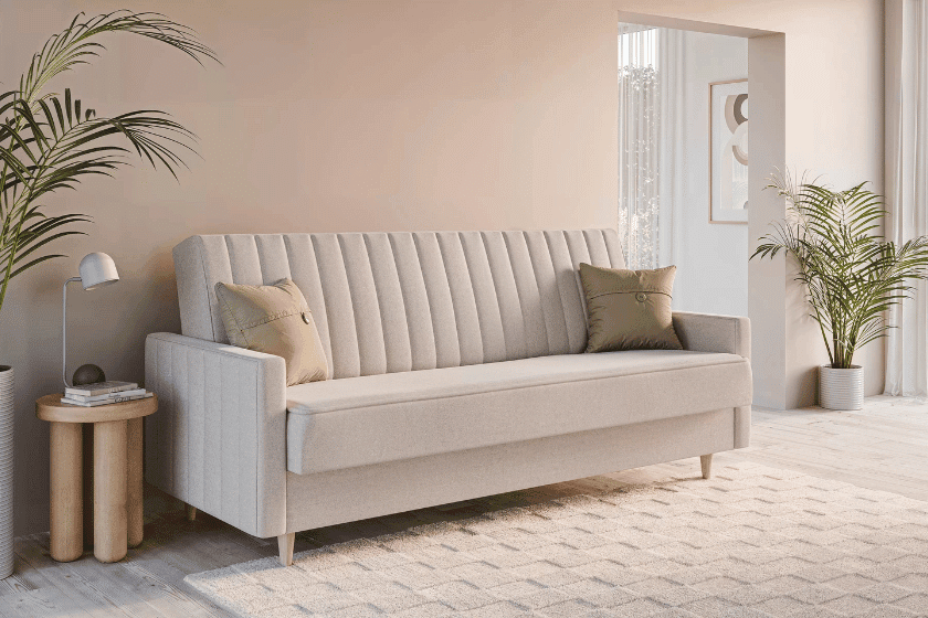 Sofa z bokami w odcieniu beżu w nowoczesnym salonie z roślinami, drewnianymi stolikami i subtelnymi dekoracjami. Posiada wygodne poduszki i tapicerkę o poziomych przeszyciach, stanowiąc elegancką część aranżacji.