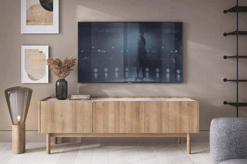 Nowoczesny salon z telewizorem na ścianie, drewnianą komodą, ozdobnymi ramkami na ścianie i dekoracyjną lampą stojącą.