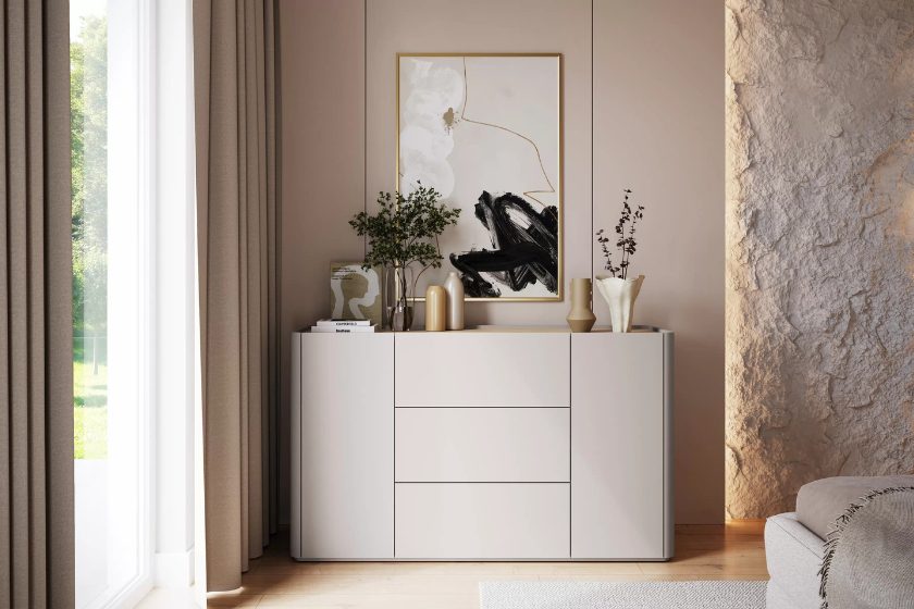 Beżowa komoda w nowoczesnej sypialni w stylu skandynawskim i boho, ustawiona przy ścianie z naturalnym wykończeniem. Na komodzie dekoracje: wazony i ramka ze sztuką nowoczesną.